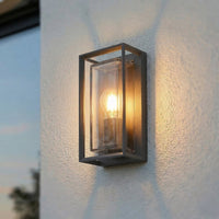Isra lantern outdoor wall light switched on at dusk on a white render wall, warm light spreading up and down with a soft crossed shadow