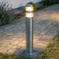 Vestro stainless steel path post light lit warm white beside a paved garden path