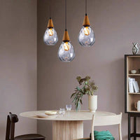 Three Drova clear glass teardrop pendants hung at staggered heights above a round dining table