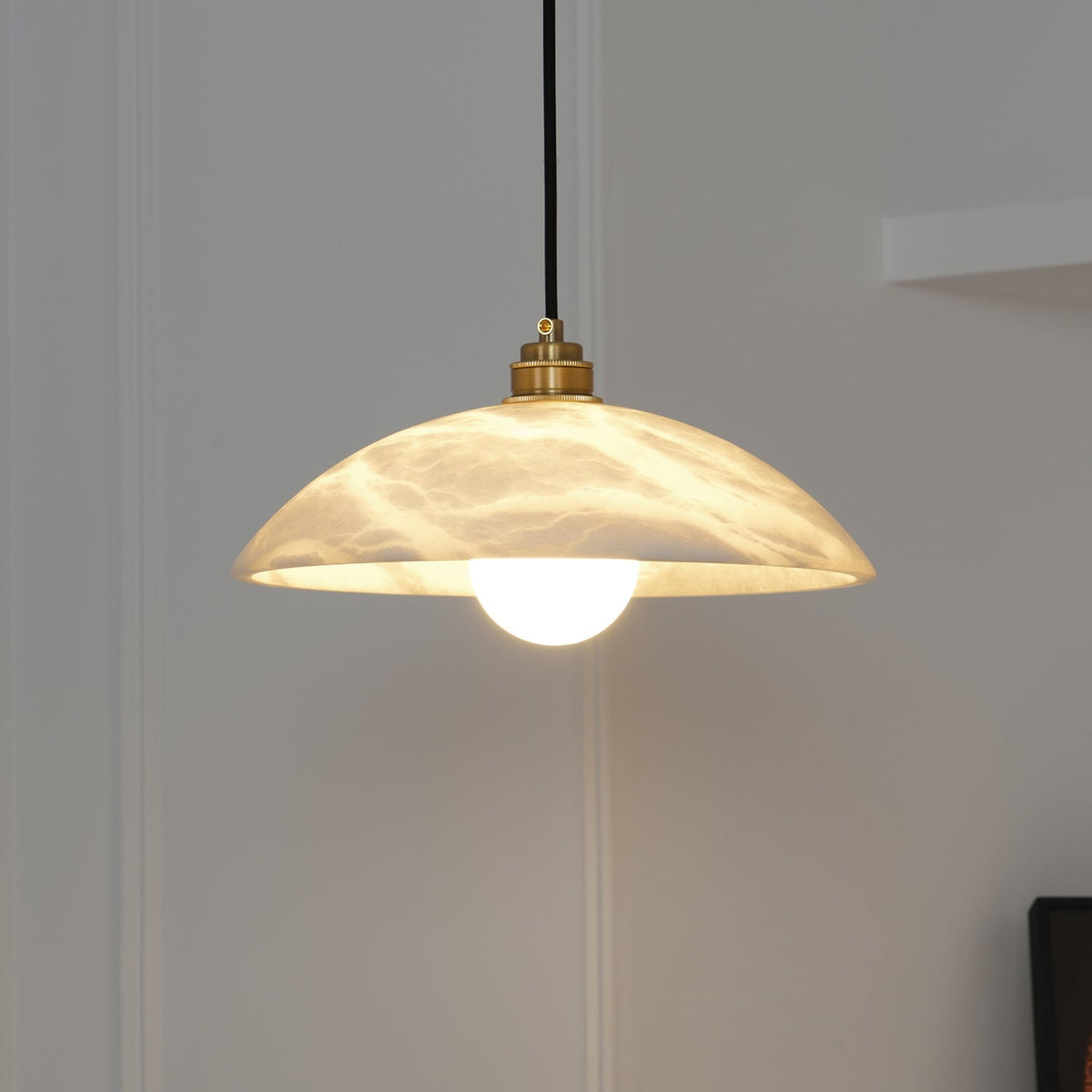 Delo alabaster pendant lit against a panelled white wall in a hallway