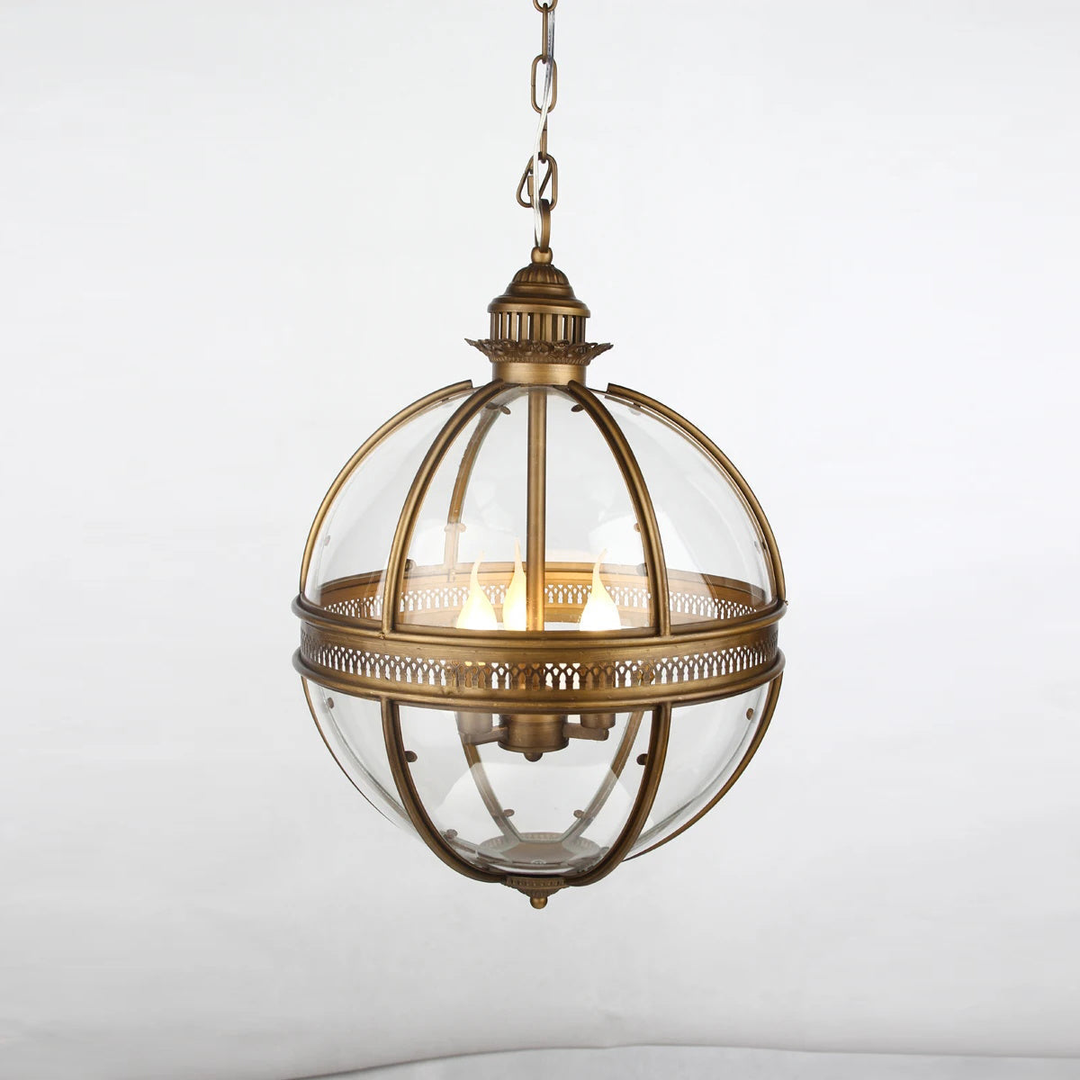 Edvo Retro Globe Pendant Light lit against a plain wall showing the aged brass fretwork band