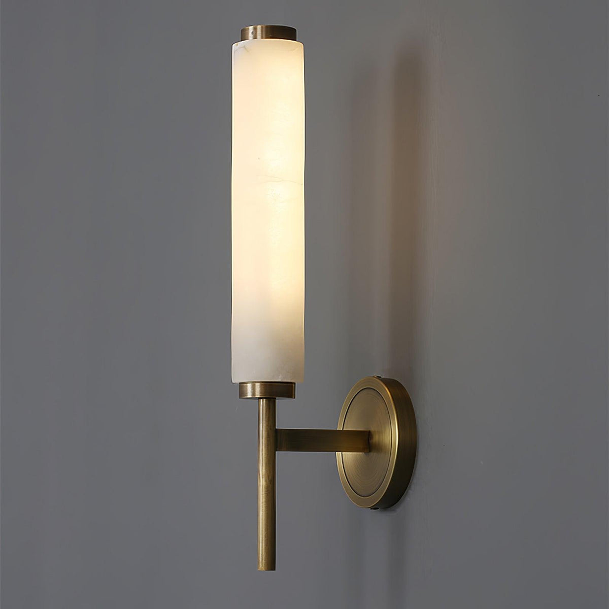 Jerno alabaster wall light lit on a grey wall showing the warm glow through the stone
