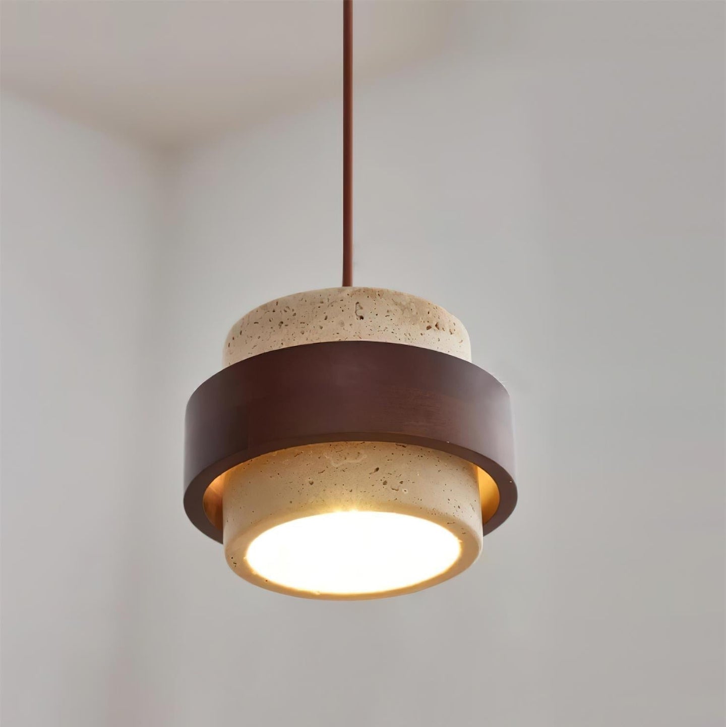 Petra travertine and walnut pendant light lit against a plain white wall