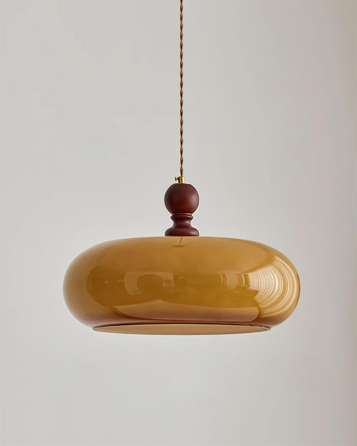 Halvo amber glass pendant light hanging against a pale grey wall on a twisted fabric cord