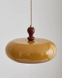 Close view of the Halvo pendant showing the turned walnut wood stem, brass fitting and glossy amber glass shade