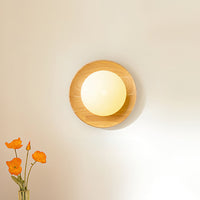 Tamso wall light lit on a pale wall, showing the glow spreading across the dished timber face