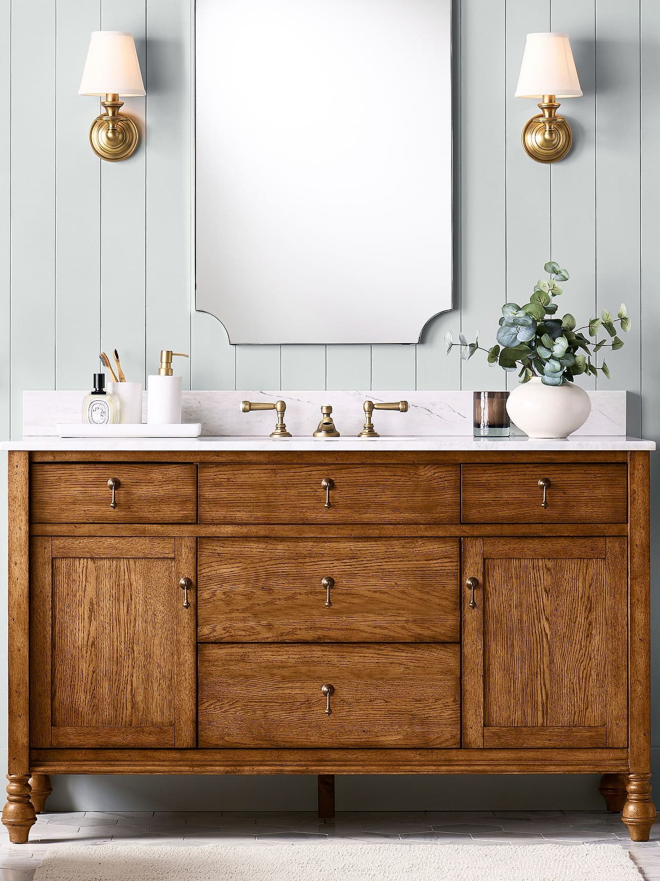 Pair of Ruva brass wall lights either side of a mirror above a wooden vanity