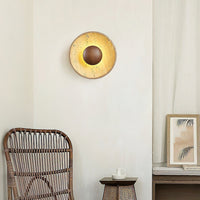 Sunda Travertine Wall Light glowing on a plaster wall beside a rattan chair and framed print