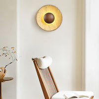 Sunda Travertine Wall Light lit above a wooden reading chair in a bright corner