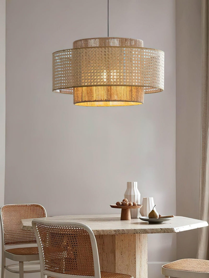 Rattan drum pendant light lit above a small dining table with woven chairs
