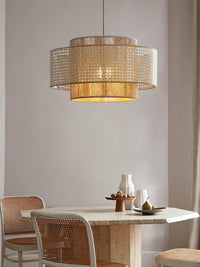Rattan drum pendant light lit above a small dining table with woven chairs