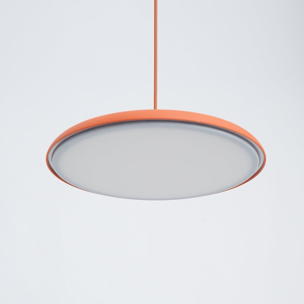 Underside view of the Tarvo orange pendant light showing the flat diffuser panel and orange rim