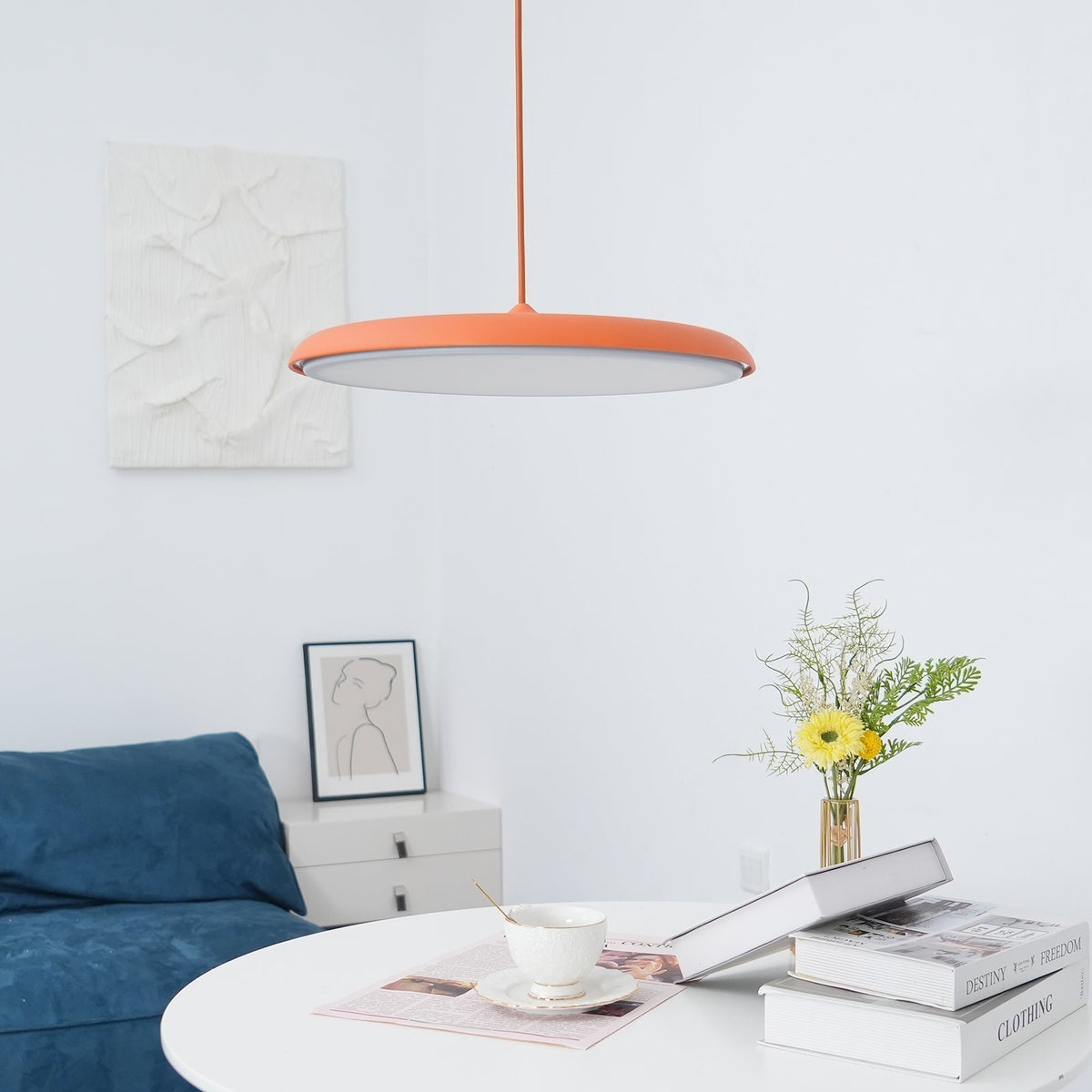Tarvo orange pendant light hanging above a white round dining table in a bright living room