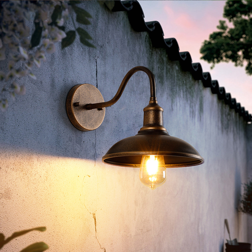 Bolva gooseneck wall light lit on a rendered courtyard wall at dusk, casting warm light down the wall