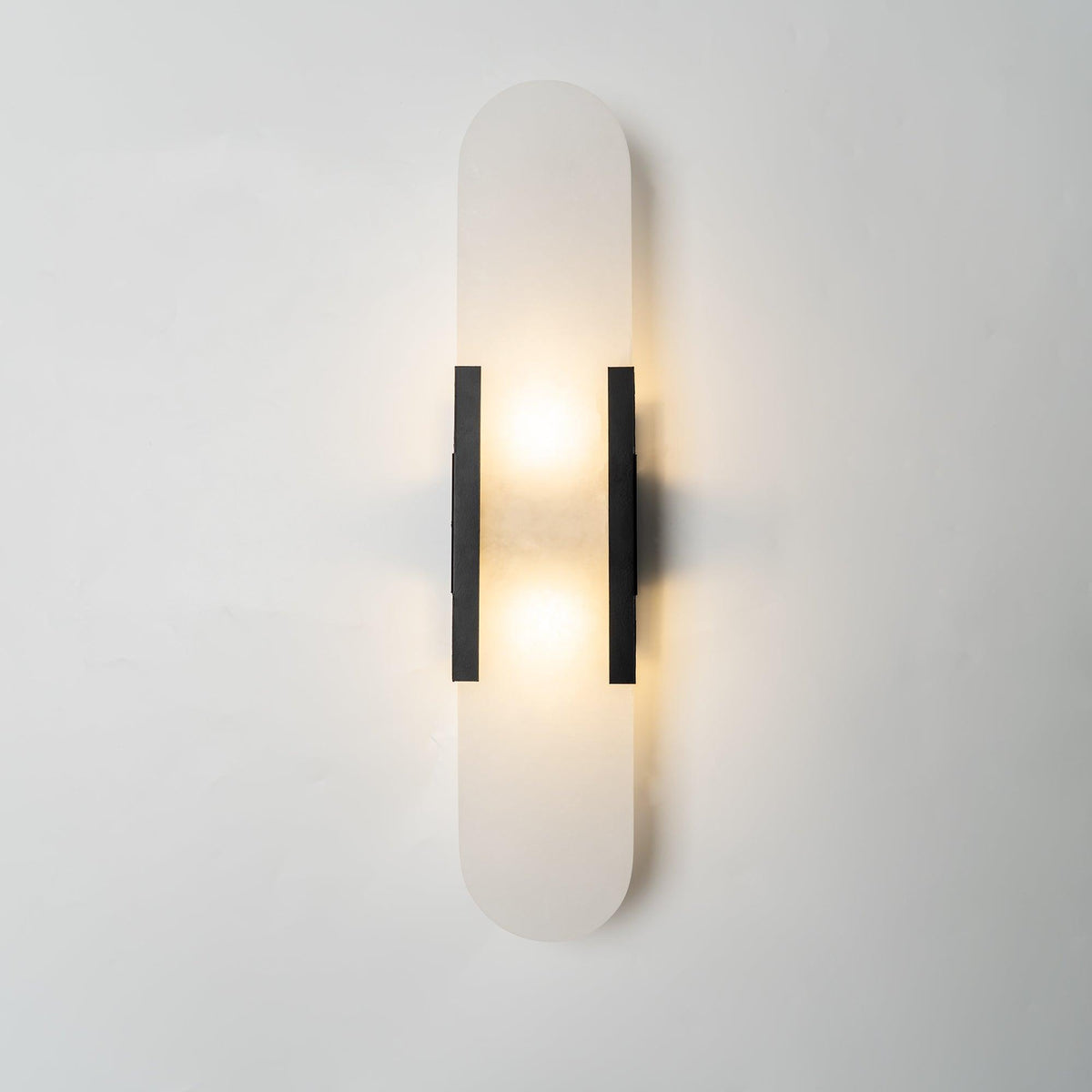 Veola wall light illuminated, with light spilling above and below the alabaster panel