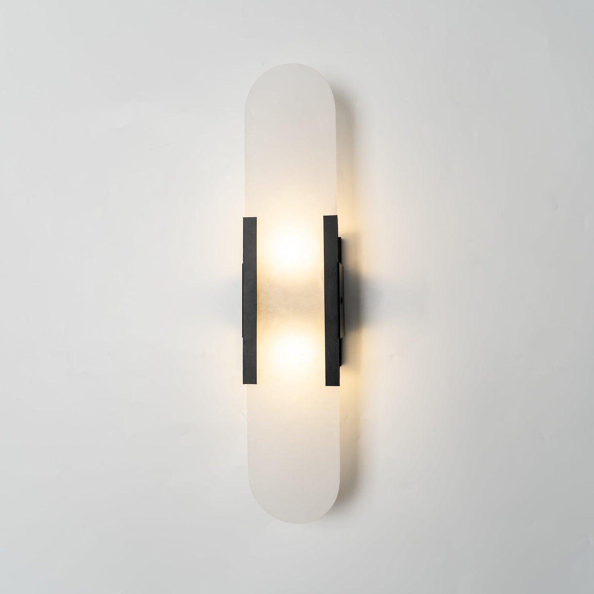 Veola alabaster wall light lit, showing warm light glowing through the natural stone