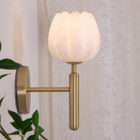 Pellora brass and alabaster wall light lit beside a lace curtain in a bedroom