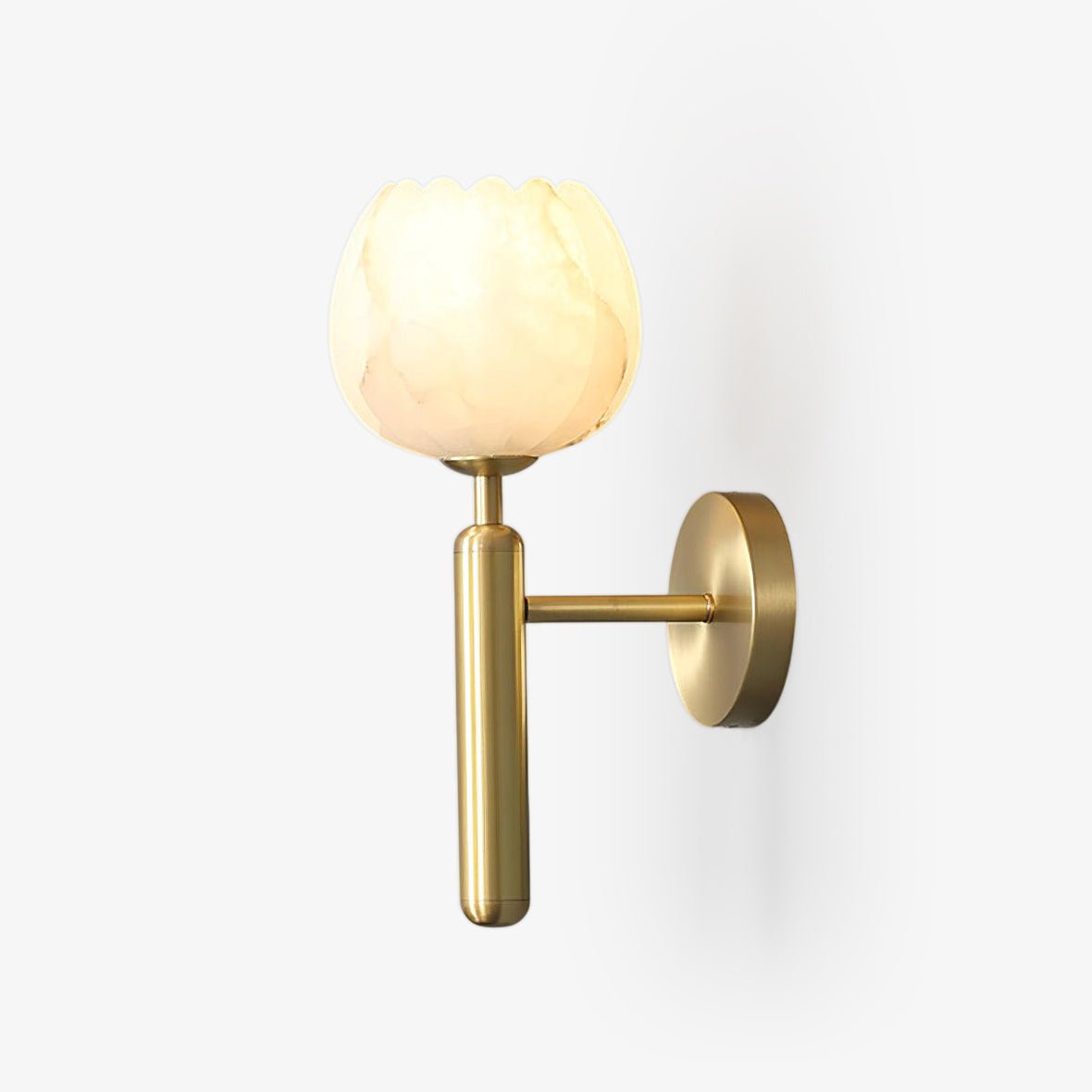 Pellora brass wall light on a plain background with the alabaster petal shade lit