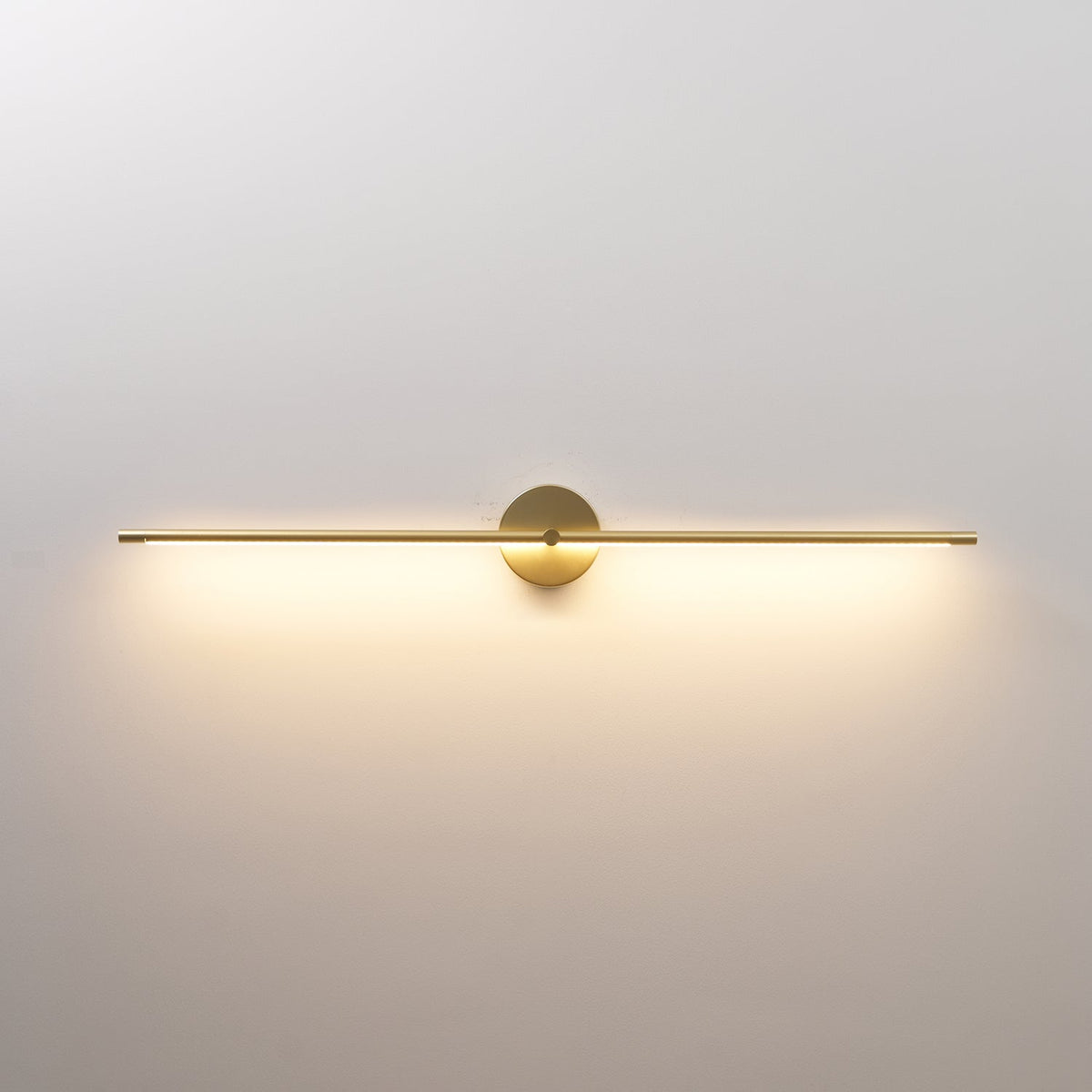 Rodo double-end linear wall light in gold, lit with a warm white glow