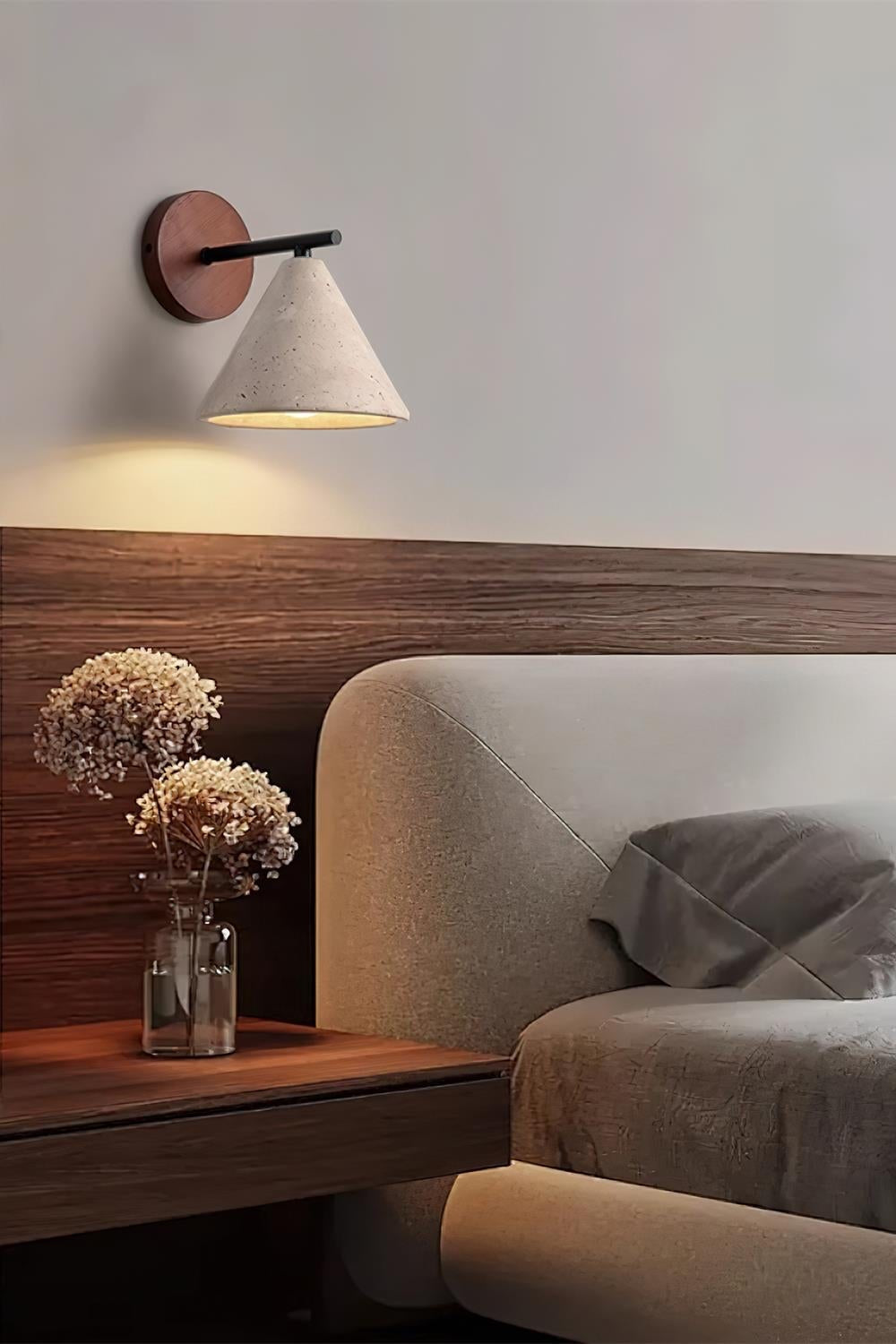 Marlo travertine wall light lit above a bedside table next to a wooden headboard