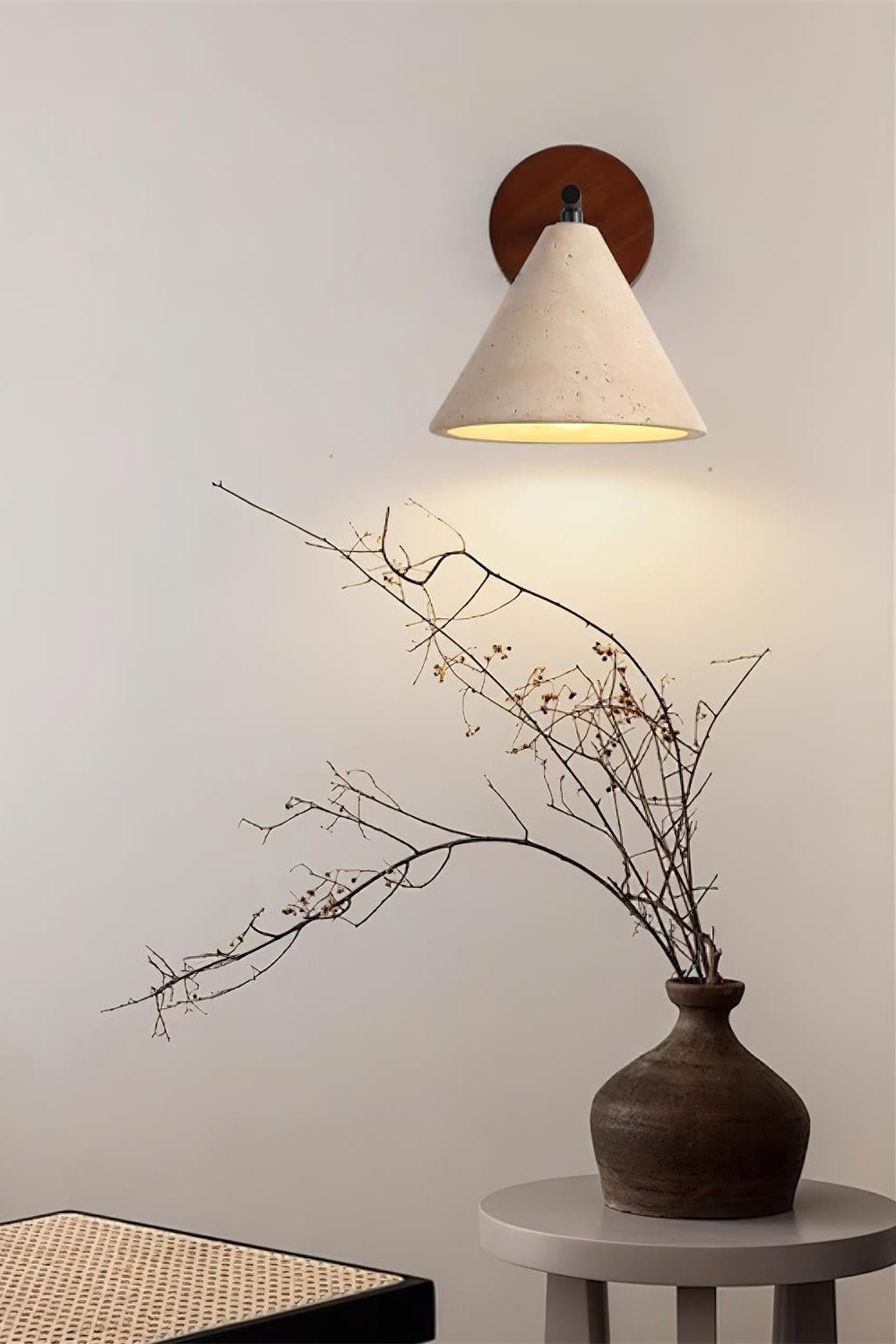 Marlo travertine wall light casting a warm wash down a plain wall above a vase of branches