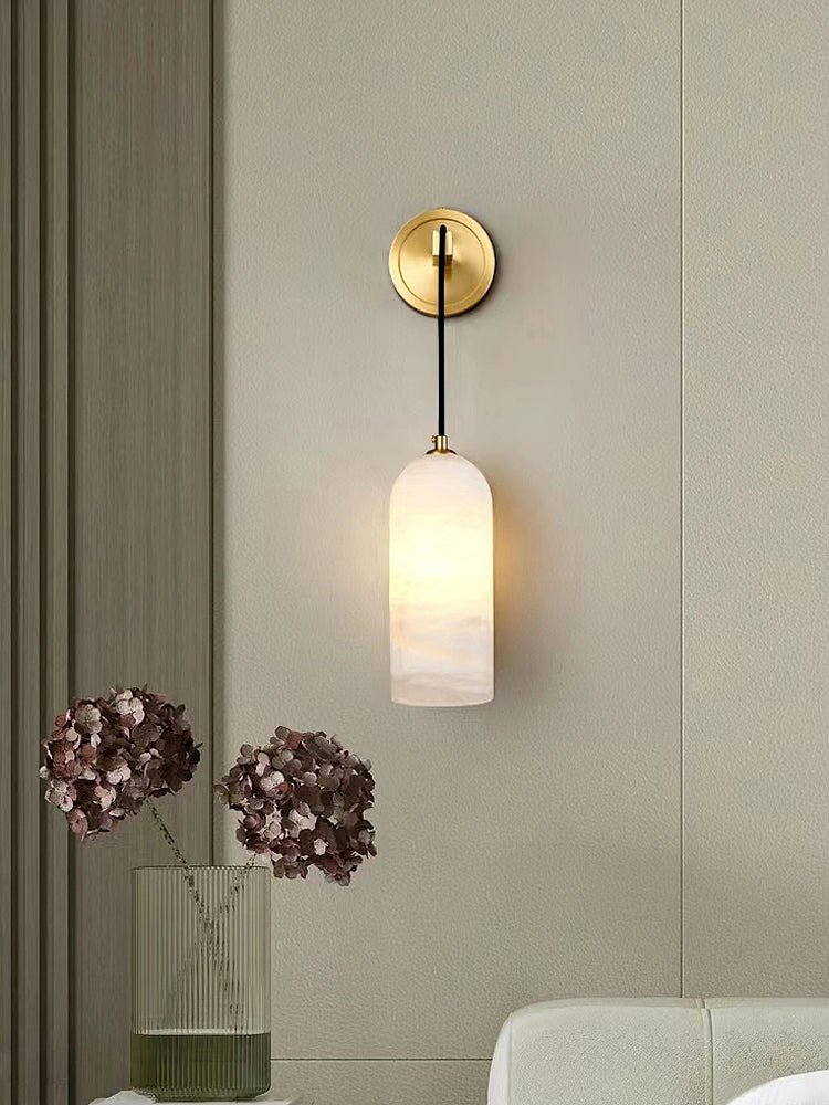 Uvella alabaster wall light mounted beside a panelled wall with a vase of flowers below