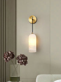 Uvella alabaster wall light mounted beside a panelled wall with a vase of flowers below