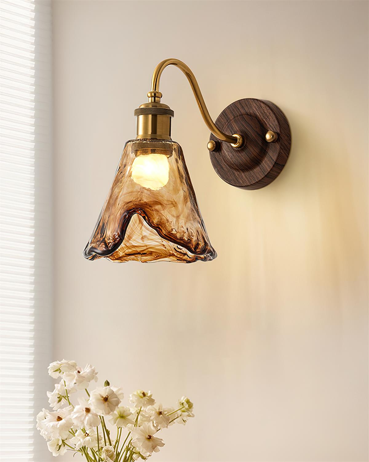 Ambro amber glass wall sconce lit on a cream wall beside a window and white flowers