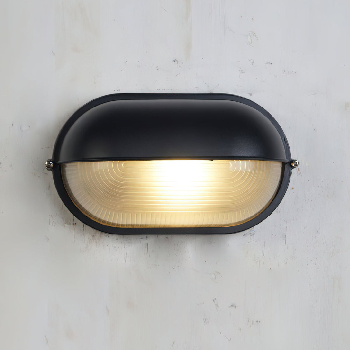 Verrow outdoor wall light lit against a concrete wall, showing the warm glow through the ribbed glass