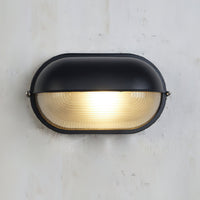 Verrow outdoor wall light lit against a concrete wall, showing the warm glow through the ribbed glass