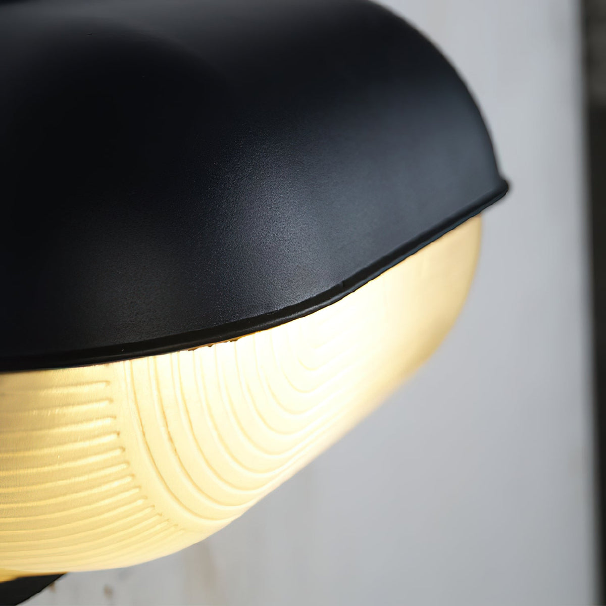 Angled detail of the black metal hood and ribbed glass lens of the Verrow outdoor wall light