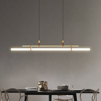 Inaro gold linear pendant hanging over a dark dining table
