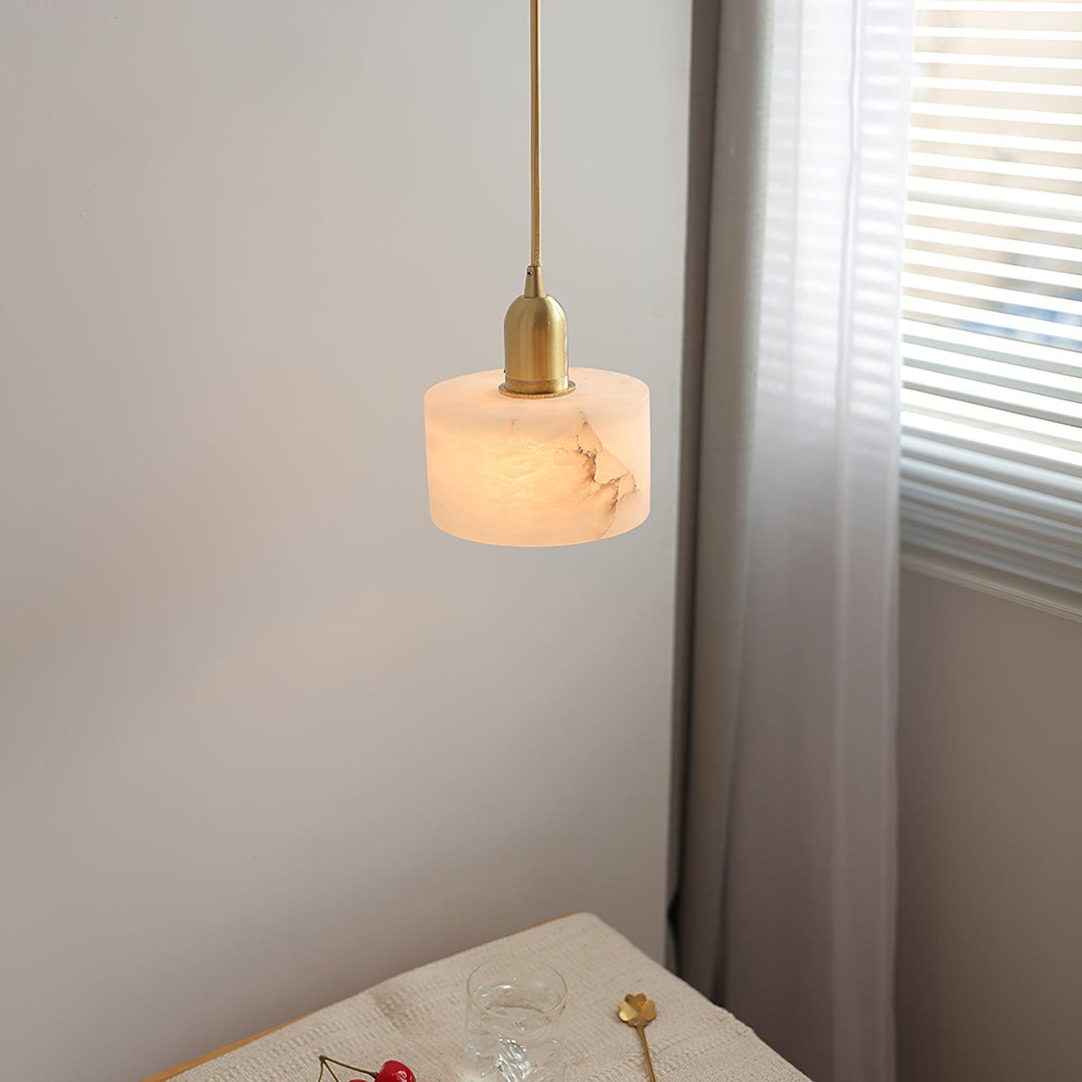 Brass and alabaster pendant light hung beside a window with curtains
