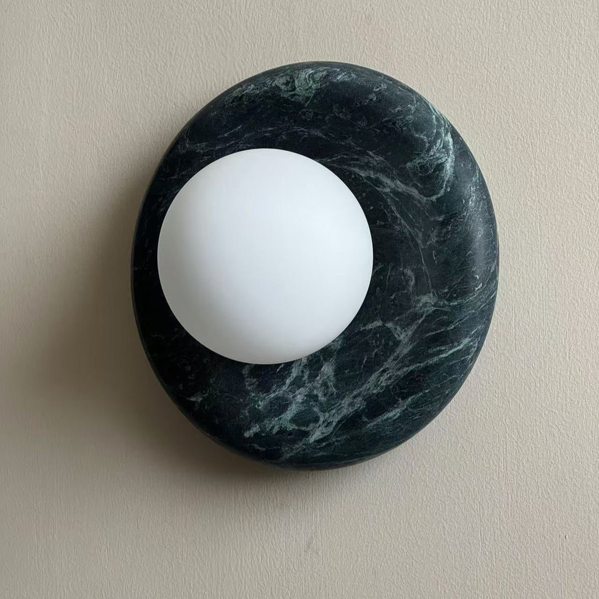 Angled view of the Avilo green marble sconce showing the rounded stone edge and offset globe