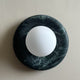 Avilo dark green marble wall sconce with a white glass globe on a plain wall