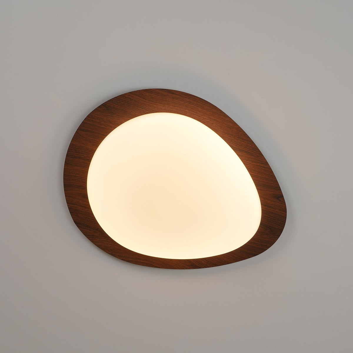 Quisto Pebble Walnut Ceiling Light lit at an angle showing the warm glow through the acrylic diffuser