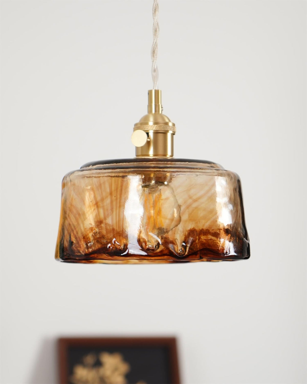 Cadro amber glass pendant lit against a plain wall showing the warm glow through the shade