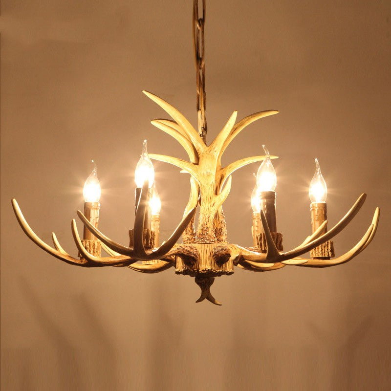 Brown antler chandelier lit with six candle bulbs against a warm wall