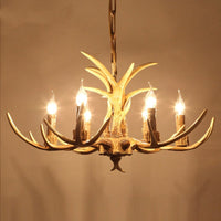 Brown antler chandelier lit with six candle bulbs against a warm wall