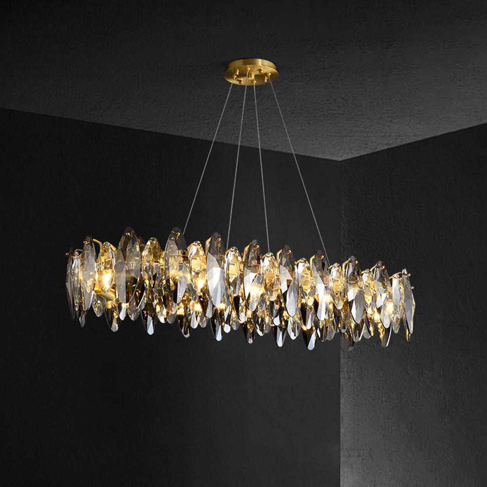 Ondra gold crystal chandelier lit in a dark room, showing the elongated silhouette and suspension wires
