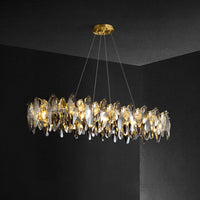 Ondra gold crystal chandelier lit in a dark room, showing the elongated silhouette and suspension wires