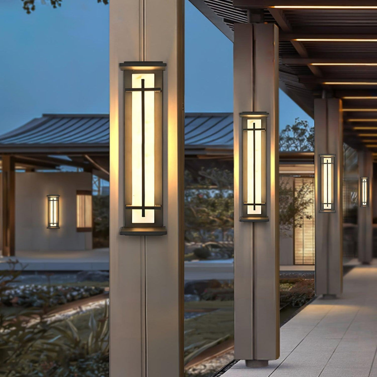 Rayo wall lights mounted on pillars along a covered outdoor walkway at dusk