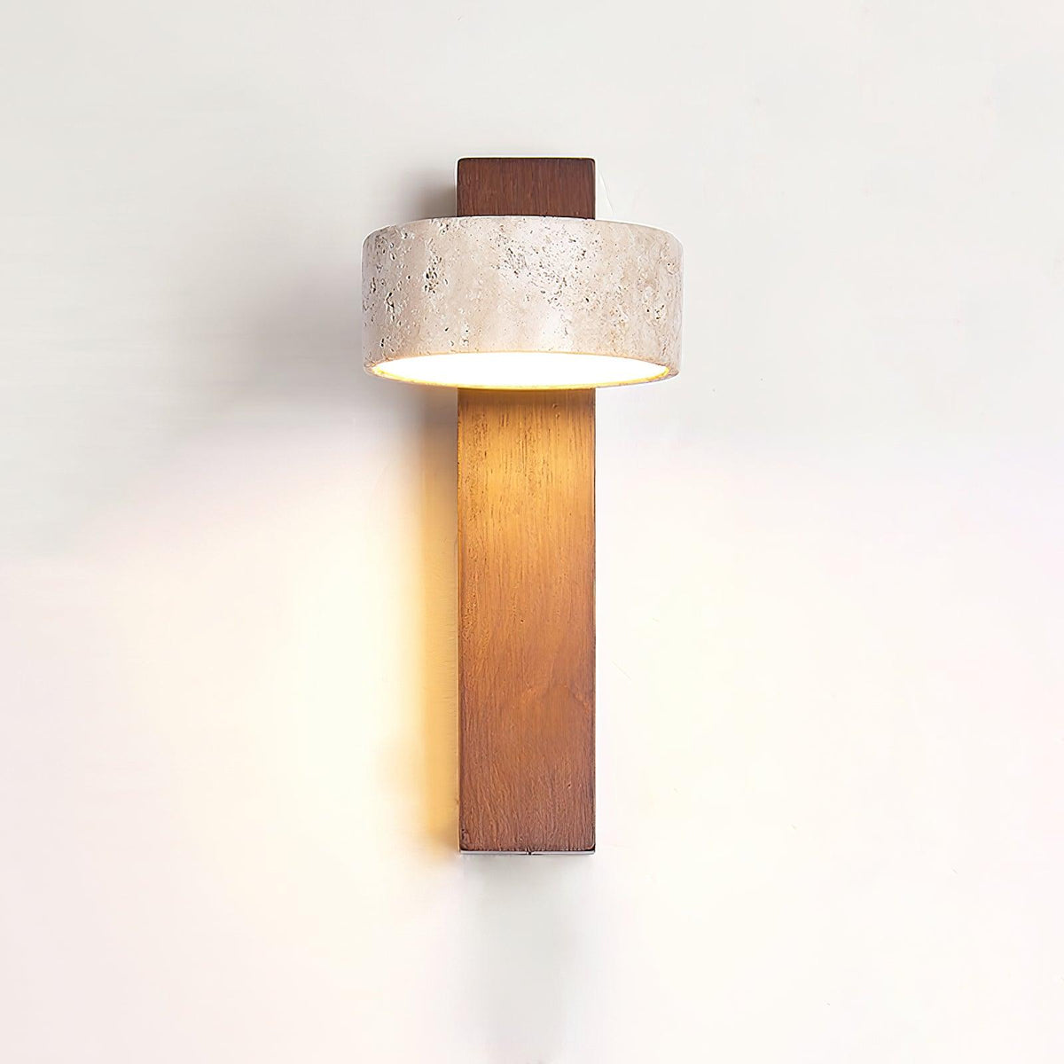 Nydo travertine wall light lit on a white wall with the stone drum set square to the walnut beam