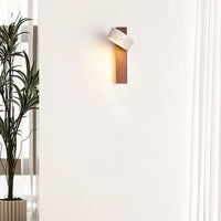 Nydo travertine wall light lit on a pale wall beside a tall indoor plant
