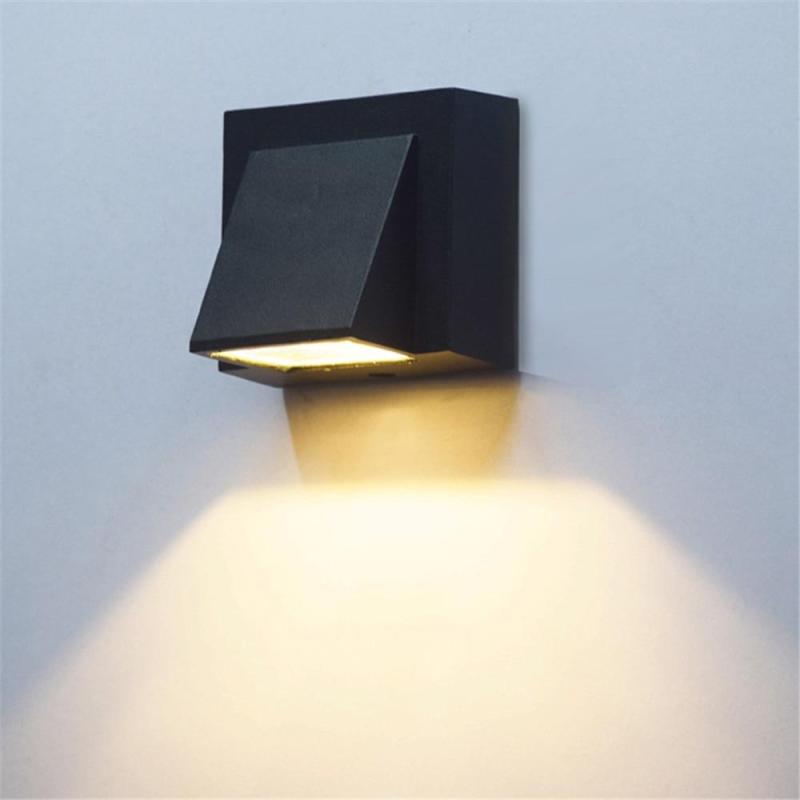 Vosto Slim Outdoor Wall Light in matt black, wedge-shaped metal body casting warm light downward on a plain wall