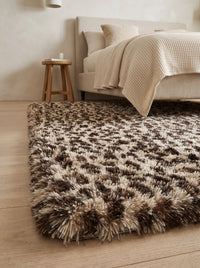 Low angle view along the edge of the Fauna Shag Rug at the foot of a linen bed, the pile depth catching soft morning daylight