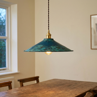 Pepa cone pendant light glowing above a rustic wooden dining table in a cream-walled room