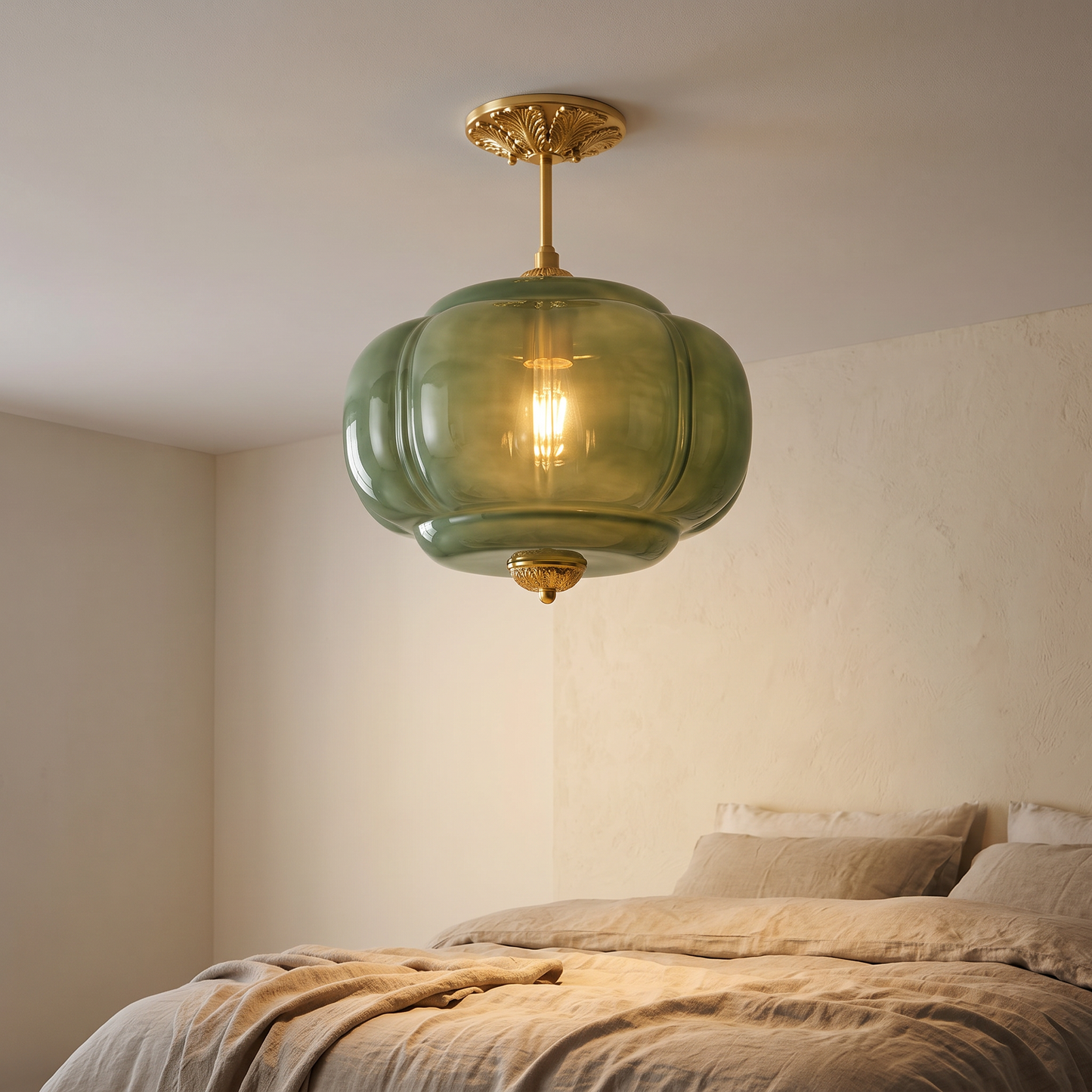 Eldo green glass ceiling light lit above a linen dressed bed in a calm cream bedroom, the ribbed sage glass glowing warm