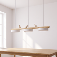 Clifo bird branch linear pendant light hanging above a light oak dining table in a bright white dining room