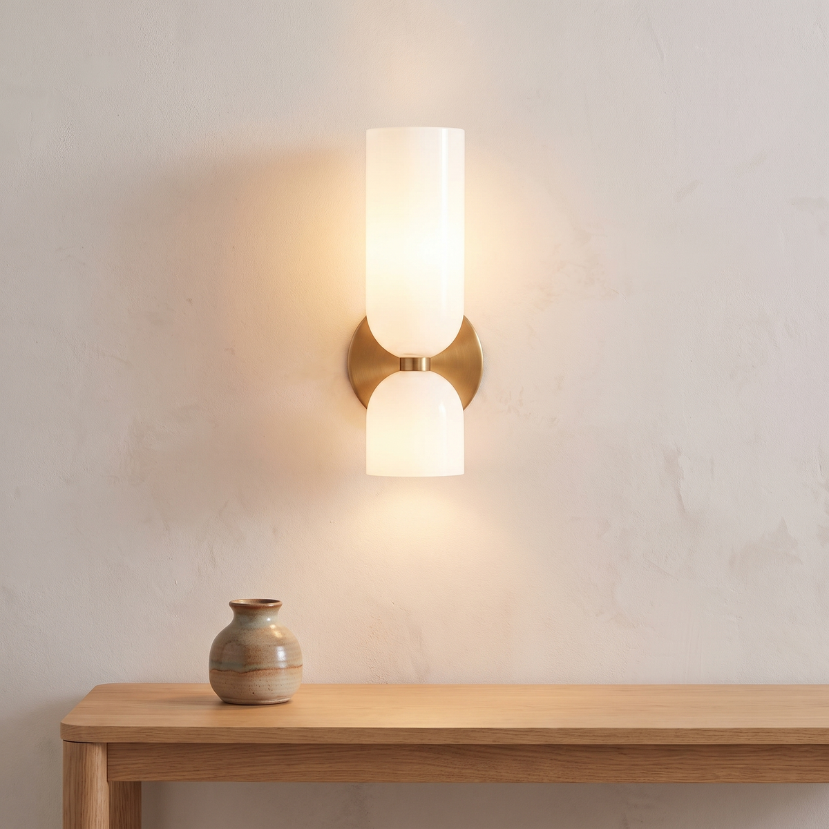 Solia Twin Glass Wall Sconce lit warm on a plaster wall above an oak table with a ceramic vase